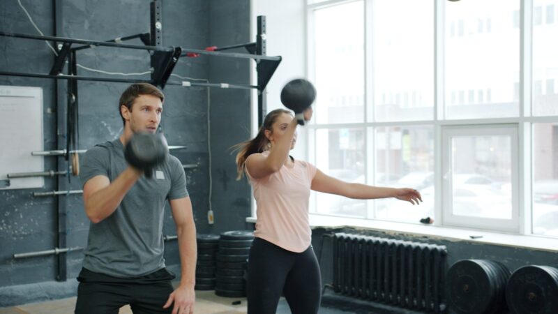 Man and woman exercising with weights in gym.